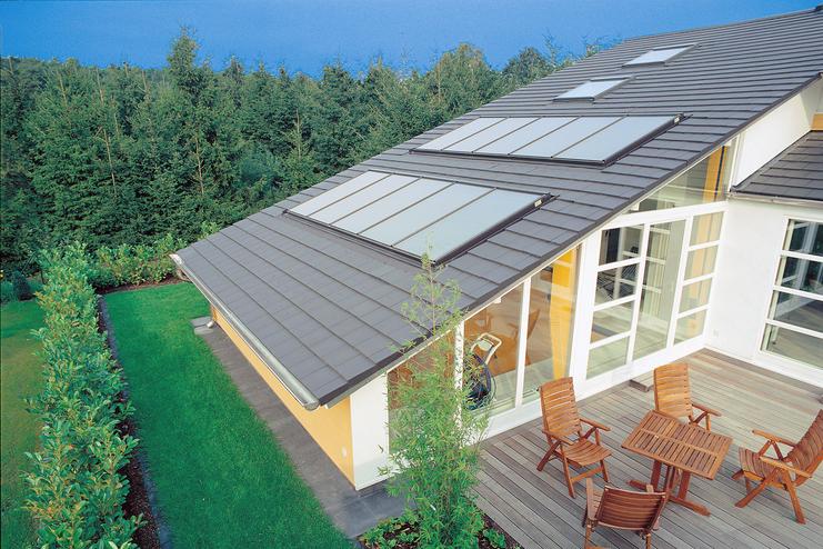 Dach eines modernen Hauses mit Fenstern, umgeben von Grünflächen und einer Holzterrasse mit Sitzmöbeln.