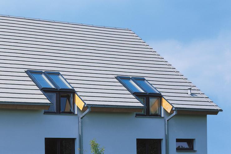 Moderne Doppelhaushälfte mit Satteldach und darunterliegenden Fenstern, umgeben von einem gepflegten Garten.